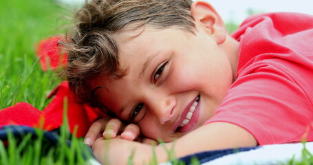 Obraz na płótnie Canvas Handsome young boy smiling to camera laid on grass outside