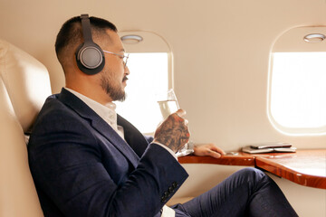 successful Asian businessman flies in private luxury jet with glass of champagne and listens to...