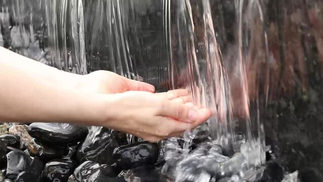 Women's hands under a stream of falling water in a fountain, a waterfall and hands