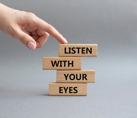 Listen with your eyes symbol. Concept word Listen with your eyes on wooden blocks. Beautiful grey background. Businessman hand. Business and Listen with your eyes concept. Copy space