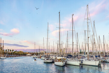 Fototapeta na wymiar Barcelona, Spain - November 26, 2021: Many yachts are moored in the Port of Barcelona in the evening on the backdrop of a pink-blue sky. Seascape of Mediterranean coastline in Barceloneta at sunset