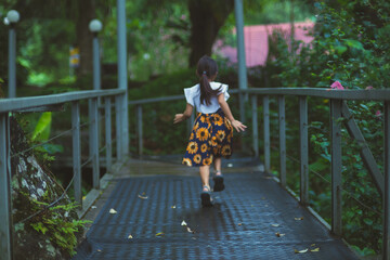 Cute little girl walking on a steel bridge in a botanical garden with green plants and colorful flowers around. Children studying nature