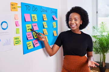 Black woman scrummaster writes on KANBAN board with ticket backlog, sprint plan