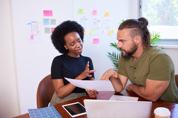 Two team members in a discussion at boardroom table, hand gestures explain