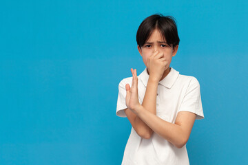 asian boy of twelve years covers his nose with his hand and avoids the stink on blue isolated background