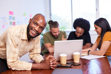 Black male manager leans against boardroom table, diverse team brainstorm