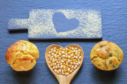 Corn kernels in heart-shaped wooden spoon. Corn flour muffins. Cornmeal on cutting board. Copy space