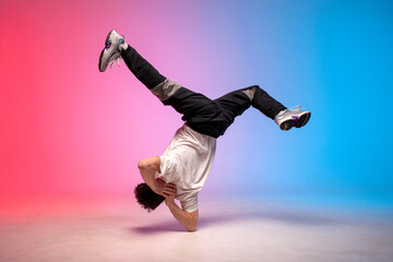 guy hiphop performer break dance in neon club lighting and doing acrobatic trick, male dancer stands in acrobatic pose
