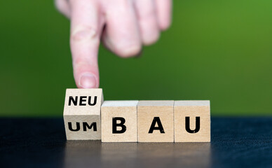 Hand turns wooden cube and changes the German expression 'Umbau' (rebuild) to 'Neubau' (new construction).