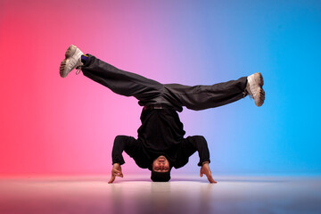 young guy hiphop performer break dancing in neon club lighting and doing acrobatic stunt, male dancer stands on his head
