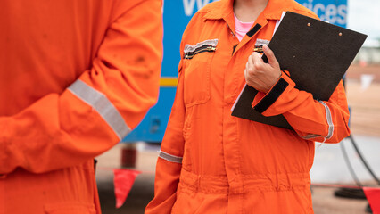 Action of a safety officer in orange coverall uniform is standing and talking with colleague during...