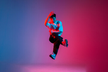 Fototapeta na wymiar male dancer jumps and flies in the air, young guy hiphop performer break dances in neon club lighting
