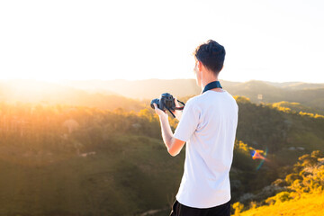 Photographer standing on top of a mountain taking pictures or filming the landscape of mountains with sunset.