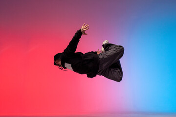 guy acrobat doing back fat in new lighting, male dancer jumps and falls in the air on red blue...