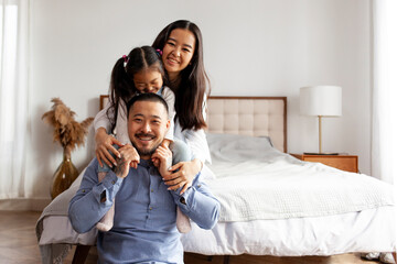 happy asian family sit together at home in the bedroom and smile, little korean girl sits on the shoulders of her dad