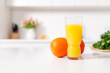 Fototapeta premium freshly squeezed orange juice in a glass stands near oranges in white modern kitchen, healthy food and drinks