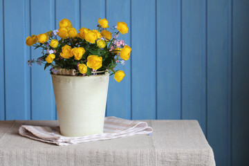 A bouquet of wildflowers in a decorative bucket on a blue background.