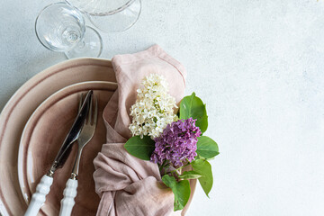Cropped table setting with lilac flowers on tableware in dust pink color on white surface