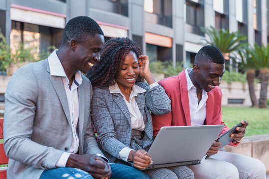 Happy black coworkers using laptop on street