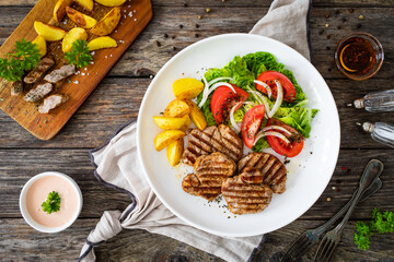 Grilled pork loin steaks with fresh vegetable salad and fried potatoes on wooden table
