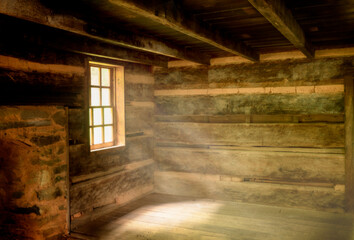 Rustic log cabin interior with light rays throughout the windows and wood floors 