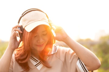 happy female asian student enjoy listen playlist music with headphone after class from school university in nature park in city with beautiful sunset light in evening