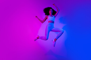 Fototapeta na wymiar Full length photo of slim funny person jumping raise fists empty space ad leggings top shoes isolated on colorful neon background