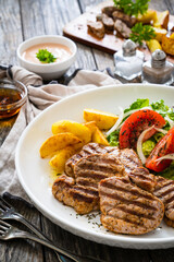 Grilled pork loin steaks with fresh vegetable salad and fried potatoes on wooden table
