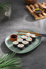 Modern japanese food concept. Maki sushi on ceramic plate with soy sauce and chopsticks on stone background. Aesthetic composition with sushi roll on dark concrete backdrop. Yin yang maki roll.