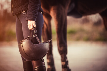 Equestrian girl standing next to her horse and holding her equestrian helmet. Equestrian sport...