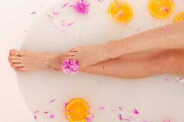 Obraz na płótnie Canvas Tender girl legs in a bath filled with fruit orange slices and flower petals. Beauty and skin care concept. Top view.