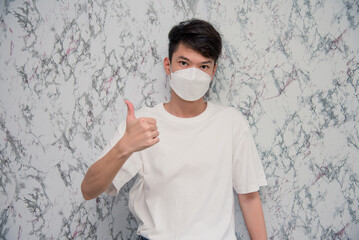 Young Man puts on a face mask showing thumbs up and looking serious isolated on White...