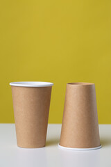 Disposable cardboard biodegradable glass on a white table, yellow background.