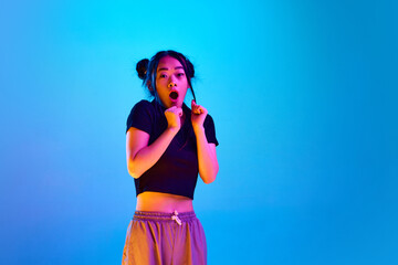 Portrait of young emotive girl showing fear, feeling scared, posing against blue studio background in neon light. Concept of emotions, facial expression, youth, lifestyle, inspiration, sales, ad