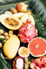 Fresh exotic fruits on green tropical palm leaves background - papaya, mango, pineapple, passion fruit, dragon fruit, watermelon. flat lay, overhead. Healthy food and diet concept. Top view.