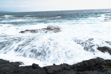 A person standing on a rock looking at waves coming up into the ocean.
