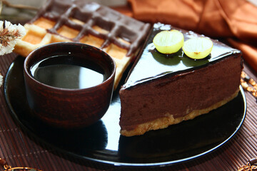 Chocolate cake, waffle, clay cup of tea, handmade pendant and white flowers on wooden background with fabric.
