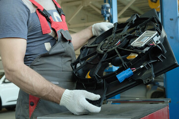 Car parts. Repair and maintenance of a passenger car in a car service center. An auto mechanic checks the integrity and serviceability of a new cooling fan before replacing it.