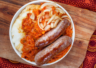 Traditional South African Pap and Wors, sausage with popular maize meal staple covered with Chakalaka or relish on wood with traditional African printed fabric