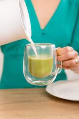 Vertical shot of a young woman pouring vegetal milk into a cup of matcha.