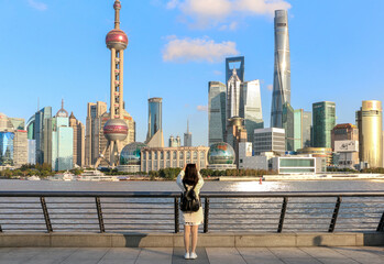 Female tourist on the Shanghai Bund taking a picture of the iconic Shanghai skyline view of Lujiazui. Shanghai a massive international city in China. - obrazy, fototapety, plakaty