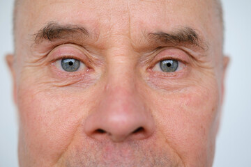 close-up of charismatic mature man, senior 60 years old looks carefully examines wrinkles on face,...