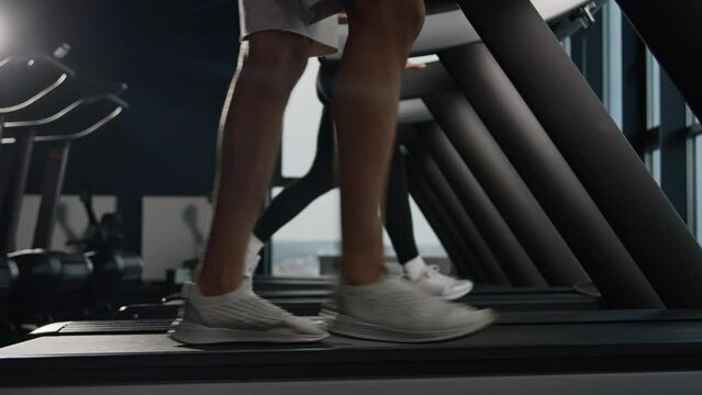 Side view legs in sneakers walk on treadmill in fitness gym unknown woman and man going footstep sport people runners walk on running machine slow stride foot step pace cardio workout health lifestyle