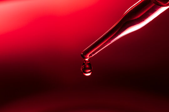 Macro science experiment pipette surface, top macro view of chemical droplet injecting oil into clear liquid in one of three petri dishes on red background. Abstract skincare cosmetics concept.