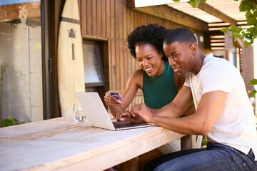 Excited Couple With Credit Card Using Laptop At Home To Book Holiday Or Shop Online