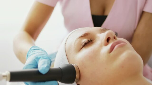 Beautician makes a procedure on the face on the cheekbones and nasolabial folds with microcurrent therapy device. Hardware cosmetology in clinic salon for client.	