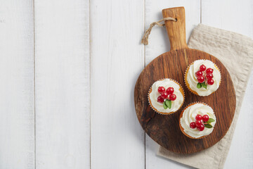 Red currant cupcakes on wooden board on white planks background