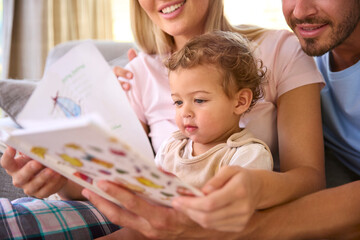 Obraz premium Family Sitting On Sofa At Home With Parents Reading Book With Young Son