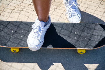 feet of african american girl stepping on a skateboard with white sneakers