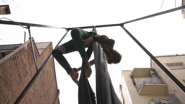 Woman on aerial fabrics in an inner courtyard of buildings, training circus and show in her house, back with tattoos and head with dreadlocks.